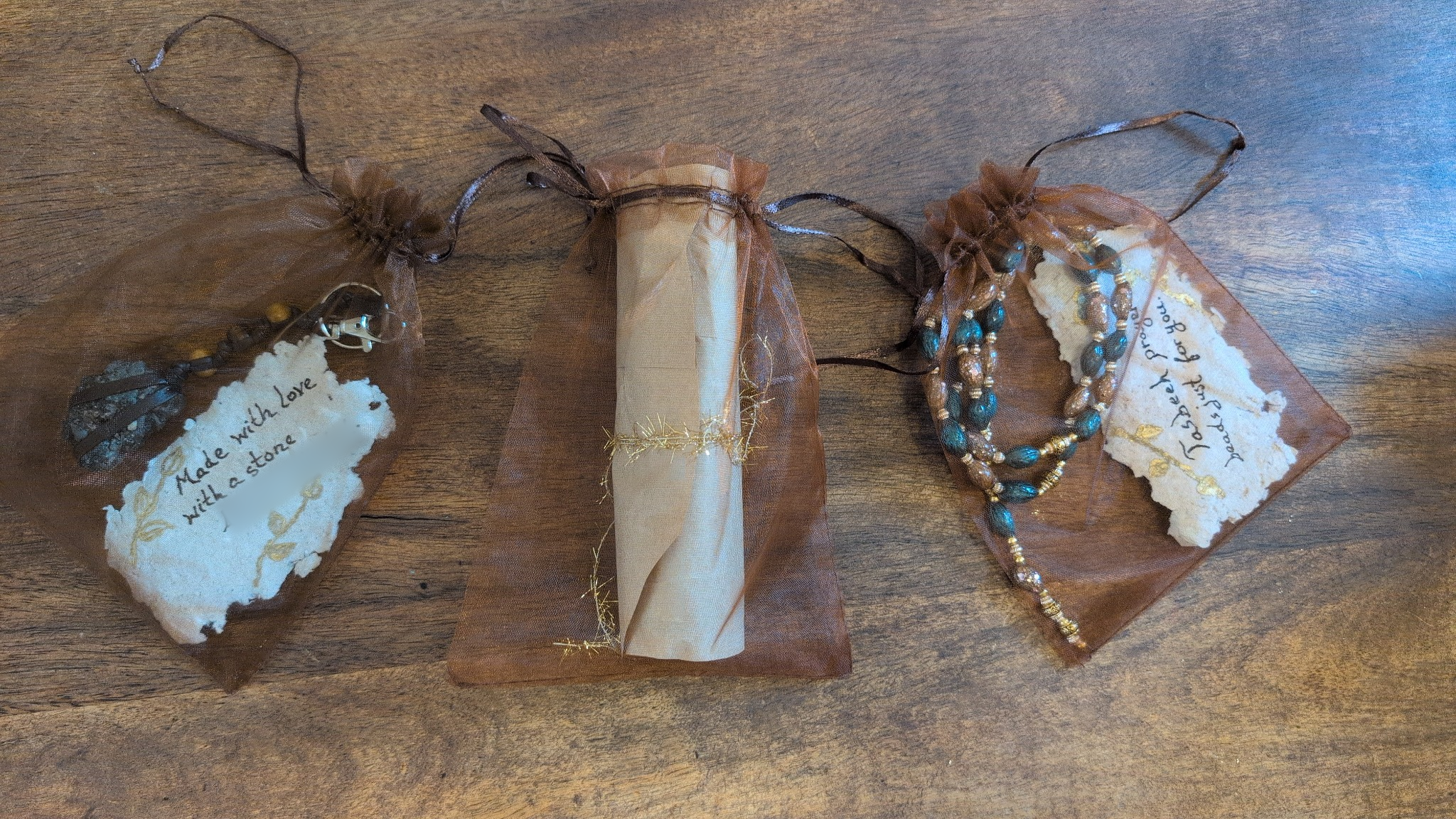 All three handmade gifts in brown pouches: a stone key chain, rolled promise note and olive-pit tasbeeh prayer beads; personal details obscured